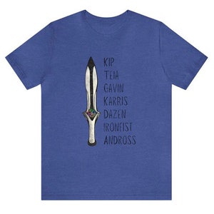 May include: Blue t-shirt featuring a detailed illustration of a dagger with a black blade and silver handle. The names Kip, Teia, Gavin, Karris, Dazen, Ironfist, and Andross are printed vertically next to the dagger.