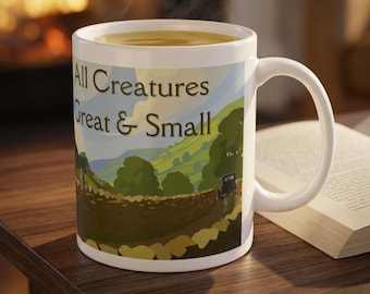 Könnte beinhalten: Ein weißer Keramikbecher mit einer Landschaftsillustration von grünen Hügeln, einer Steinmauer und einem Oldtimer. Der Text All Creatures Great & Small ist in dunkelbraunen Buchstaben mittig auf dem szenischen Design aufgedruckt.