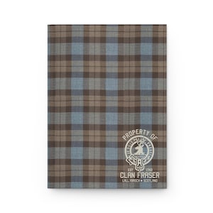 May include: A brown and blue tartan notebook cover with a white crest featuring a stag and the text "Property of Clan Fraser Est. 1743 Lallybroch Scotland".