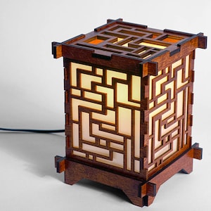 May include: A wooden table lamp with a geometric design. The lamp has a warm, white light that shines through the intricate pattern.