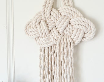 May include: A white macrame wall hanging with a knotted design and a fringe of tassels.