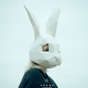 May include: A person wearing a white origami bunny mask. The text "THE MASK SHAME COVER" is printed below the mask.