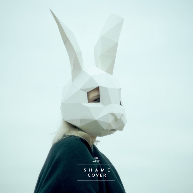 May include: A person wearing a white origami bunny mask. The text "THE MASK SHAME COVER" is printed below the mask.
