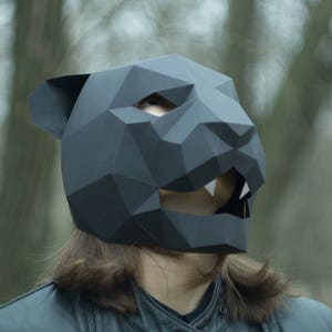 Op de afbeelding: Een zwart papieren masker van een panter met een geometrisch ontwerp. Het masker heeft een scherpe, hoekige uitstraling en is gemaakt van gevouwen papier.