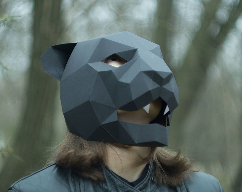 Op de afbeelding: Een zwart papieren masker van een panter met een geometrisch ontwerp. Het masker heeft een scherpe, hoekige uitstraling en is gemaakt van gevouwen papier.