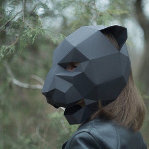 Op de afbeelding: Een persoon draagt ​​een zwart origami-pantermasker. Het masker is gemaakt van papier en heeft een geometrisch ontwerp.