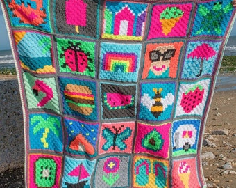 Pode incluir: Uma manta de crochê colorida com vários quadrados temáticos de verão, incluindo uma melancia, um cone de sorvete, uma palmeira, uma borboleta e um guarda-sol de praia.