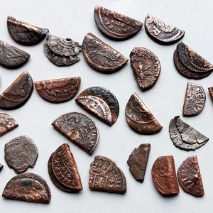 Puede incluir: Una colección de 28 monedas antiguas de cobre y plata. Las monedas están todas en varios estados de desgaste y rotura, algunas muestran signos de daño. Las monedas están dispuestas en un patrón aleatorio sobre una superficie blanca.