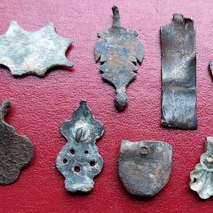 May include: A collection of eight antique metal pendants in various shapes and designs. The pendants are made of different metals, including silver, copper, and bronze. Some of the pendants have intricate details, while others are more simple. The pendants are all in good condition, despite their age.