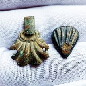 May include: Two antique bronze pendants, one shaped like a scallop shell with a loop at the top, the other shaped like a teardrop with a ribbed design.