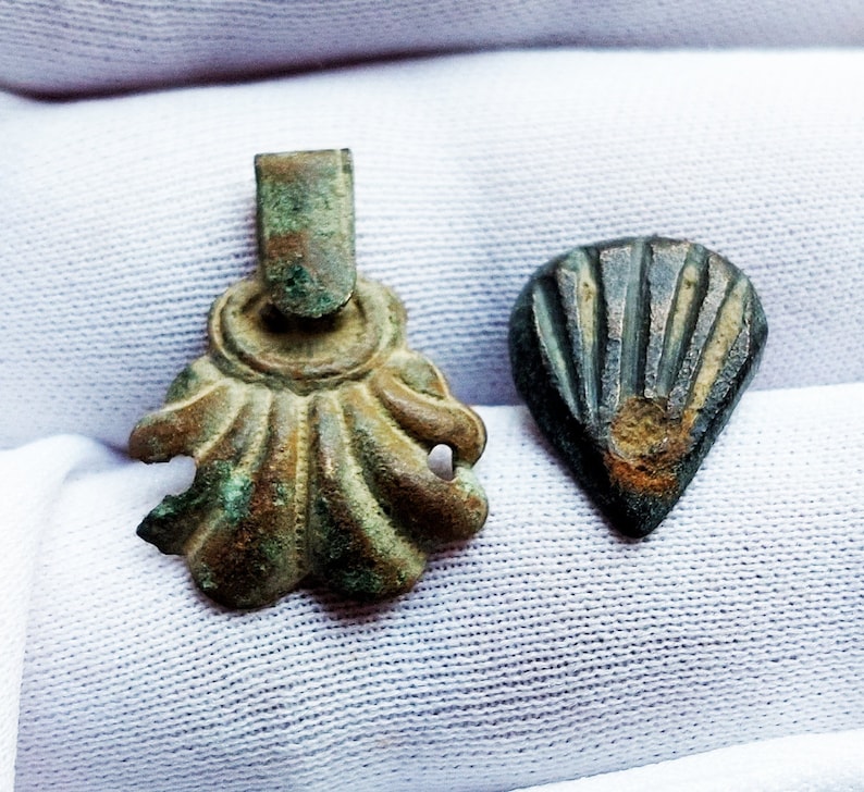 May include: Two antique bronze pendants, one shaped like a scallop shell with a loop at the top, the other shaped like a teardrop with a ribbed design.