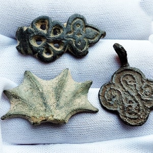 May include: Three antique bronze pendants with intricate designs. The first pendant is a four-leaf clover with a central hole. The second pendant is a starburst shape with a raised center. The third pendant is a stylized flower with a central hole.