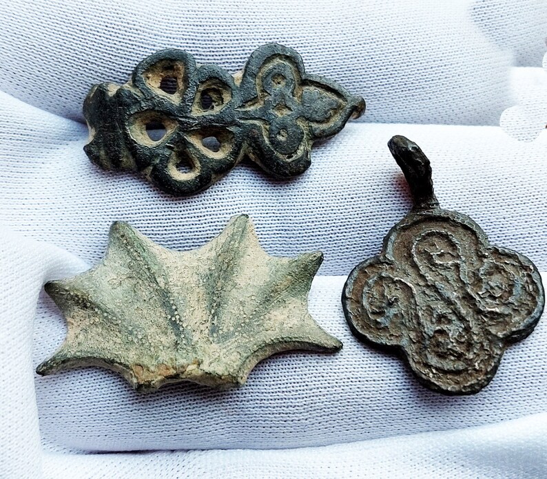 May include: Three antique bronze pendants with intricate designs. The first pendant is a four-leaf clover with a central hole. The second pendant is a starburst shape with a raised center. The third pendant is a stylized flower with a central hole.