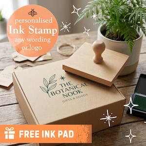 May include: A square wooden ink stamp with a rounded handle resting on a brown cardboard box. The box features a green printed logo with a leaf illustration and the text THE BOTANICAL NOOK GIFTS & GOODS. A black ink pad is visible nearby.