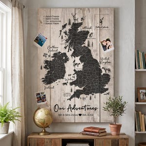 Puede incluir: Un mapa de madera de las Islas Británicas con un contorno gris oscuro de los países y condados. El mapa tiene las palabras "Our Adventures" y "Mr & Mrs Jones Est. 2002" impresas. Las fotos están sujetas al mapa.