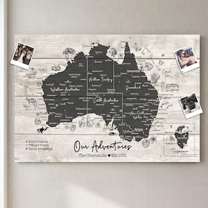 May include: A wooden map of Australia with a dark grey outline, featuring city names and illustrations. The text "Our Adventures" and "The Chernaults Est 2001" is displayed. The map has attached photographs, and is mounted on a wooden background.