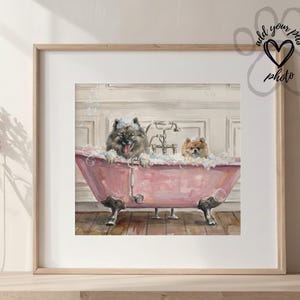 Op de afbeelding: Ingelijste illustratie van twee honden in een roze badkuip met klauwpoten, gevuld met bellen. De honden, één grijs en één bruin, genieten van een bad. Het kunstwerk staat tegen een witte achtergrond met een vintage kraan.