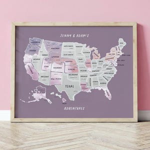 Puede incluir: Un mapa enmarcado de los Estados Unidos con cada estado etiquetado. El mapa está en tonos de morado, rosa y gris, con el texto "Jenny & Adam's Adventures" en la parte superior e inferior. El marco es de color madera clara.