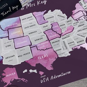 May include: A personalised scratch-off travel map of the USA, with states in shades of purple and grey. The map includes state names and is labelled "USA Adventures." A rolled-up map with text is in the upper left.
