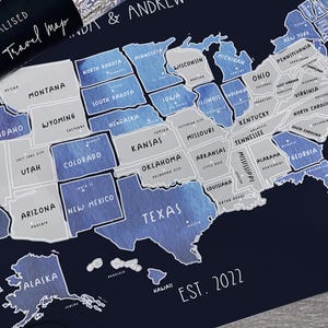 May include: A personalised scratch-off travel map of the United States, with each state outlined in white and filled with a blue watercolour design. The map includes the text "PERSONALISED Scratch Travel map" and "EST. 2022".