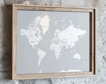 May include: A framed world map print with a light gray background and white detailing of countries and cities. The map is encased in a light brown wooden frame, suitable for home or office decor.