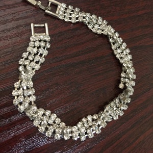 May include: A silver bracelet featuring a delicate design of clear rhinestones. The bracelet is made up of multiple rows of stones set in a wavy pattern.
