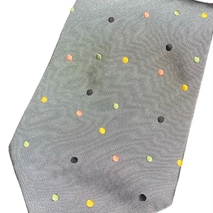 May include: A gray necktie with a repeating pattern of colorful polka dots. The dots are in shades of yellow, orange, green, and black. The tie is made of a smooth fabric and is angled towards the viewer.