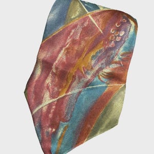May include: Abstract patterned necktie in shades of red, blue, and gold. The tie features a diagonal design with brushstroke-like patterns. The fabric has a slight sheen, suggesting a silk or satin material. The tie is a classic accessory.
