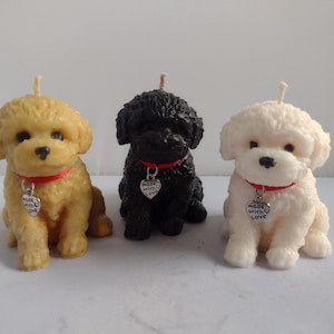 May include: Three dog-shaped candles in yellow, black, and white. Each candle has a red collar with a heart-shaped charm that reads "Made with Love." The candles have a textured appearance and a wick on top.