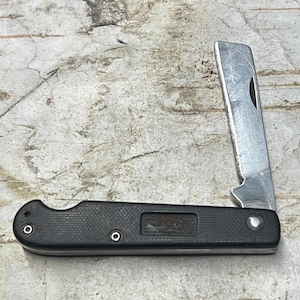 May include: A black folding knife with a silver blade is partially open. The handle is textured and has two small silver rivets. The blade is a shiny silver color and has a small notch near the top.