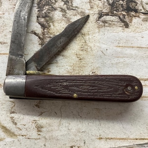 May include: A vintage pocket knife with a dark brown handle and two open blades. The blades are made of metal and show signs of wear. The handle is textured and secured with brass rivets.