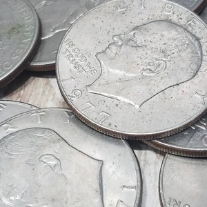 May include: A close-up of a stack of silver US dollar coins. The coins are from 1977 and 1979. The coins feature the profile of a man's face and the words "In God We Trust".
