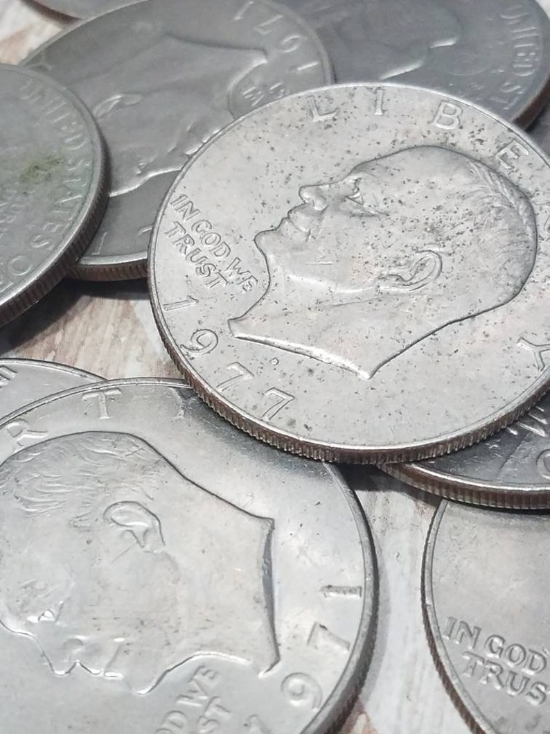 May include: A close-up of a stack of silver US dollar coins. The coins are from 1977 and 1979. The coins feature the profile of a man's face and the words "In God We Trust".