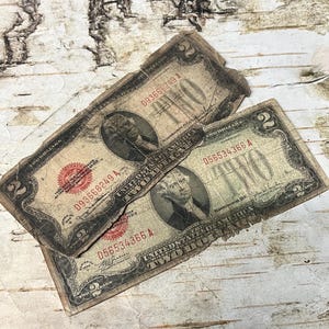 May include: Two vintage two-dollar bills, slightly worn, are displayed. Each bill features a portrait of a man and the text "TWO DOLLARS". The bills have a red seal and black text, with serial numbers visible.