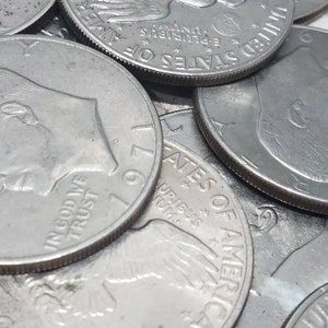 May include: A close-up of a stack of silver US half dollar coins. The coins feature the image of an eagle with the words "In God We Trust" and "United States of America" visible. The coins are dated 1971.