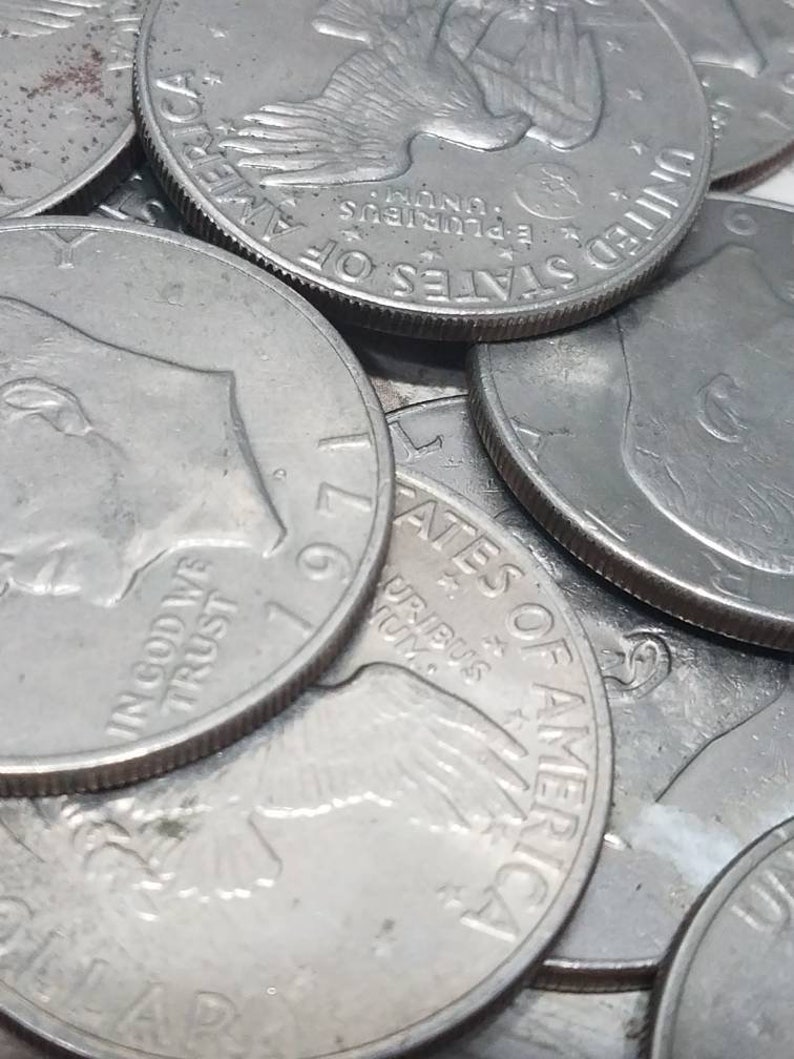 May include: A close-up of a stack of silver US half dollar coins. The coins feature the image of an eagle with the words "In God We Trust" and "United States of America" visible. The coins are dated 1971.
