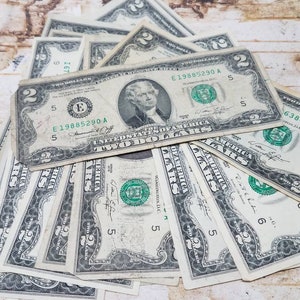 May include: A stack of ten two dollar bills, all with the same serial number, E19885290 A. The bills are arranged in a fan shape, with the top bill facing the viewer. The bills are all in good condition, with no visible tears or creases.