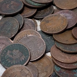Pu&ograve; includere: Una collezione di antiche monete da un centesimo di dollaro USA, con varie date e disegni. Le monete mostrano segni di et&agrave;, con una miscela di patina marrone e verde. Alcune monete mostrano il testo "ONE CENT" e "UNITED STATES OF AMERICA".
