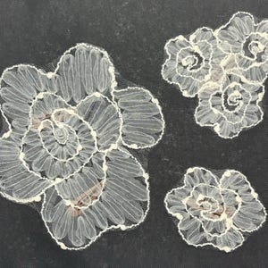 May include: Three white lace flower appliques with a delicate, intricate design. The appliques are perfect for adding a touch of elegance to any project.
