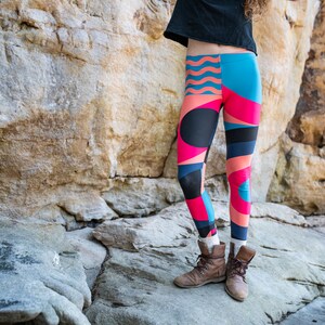 Op de afbeelding: Een persoon draagt ​​kleurrijke leggings met geometrische patronen in tinten roze, blauw en zwart. De leggings worden gecombineerd met bruine enkellaarsjes.