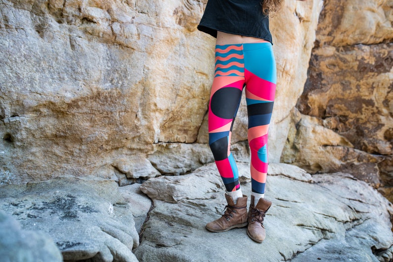 Op de afbeelding: Een persoon draagt ​​kleurrijke leggings met geometrische patronen in tinten roze, blauw en zwart. De leggings worden gecombineerd met bruine enkellaarsjes.
