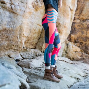 Op de afbeelding: Een persoon draagt kleurrijke leggings met geometrische patronen in tinten roze, blauw en zwart. De leggings worden gedragen met bruine enkellaarsjes.