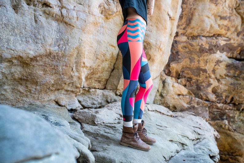 Op de afbeelding: Een persoon draagt kleurrijke leggings met geometrische patronen in tinten roze, blauw en zwart. De leggings worden gedragen met bruine enkellaarsjes.