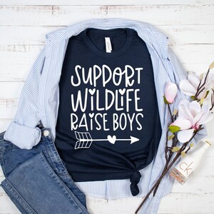 May include: A navy blue t-shirt with white text that reads "Support Wildlife Raise Boys" with a white arrow and heart graphic.