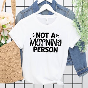 Pu&ograve; includere: Maglietta bianca con testo nero che dice "Not a Morning Person".