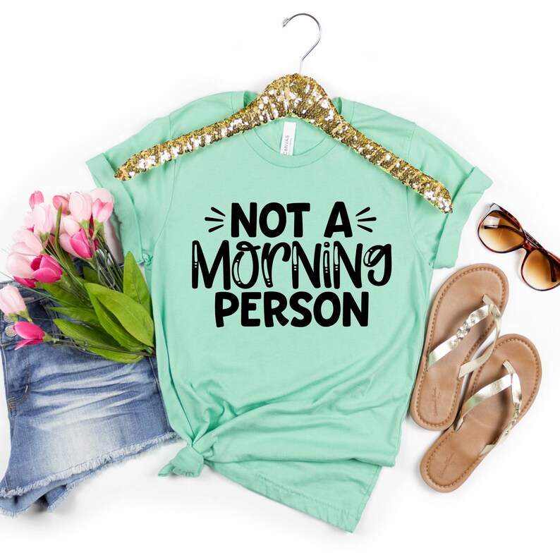 Pu&ograve; includere: Una maglietta verde menta con il testo "NOT A MORNING PERSON" in lettere nere.