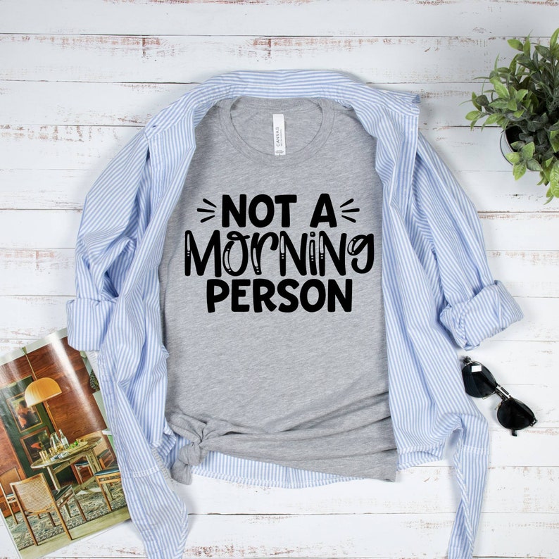 Pu&ograve; includere: Una maglietta grigia con il testo "Not a Morning Person" in lettere nere.