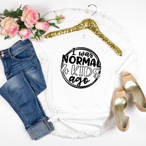 May include: White t-shirt with black text that reads "I was normal 4 kids ago" in a circle.