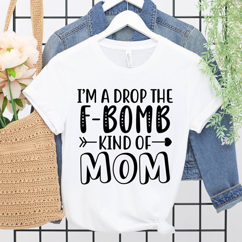 May include: White t-shirt with black text that reads "I'm a drop the F-bomb kind of mom" with an arrow pointing to the right and a heart.