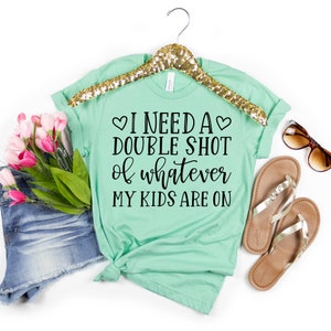 May include: A light green t-shirt with the text "I need a double shot of whatever my kids are on" printed on it. The text is in black and includes two small hearts.